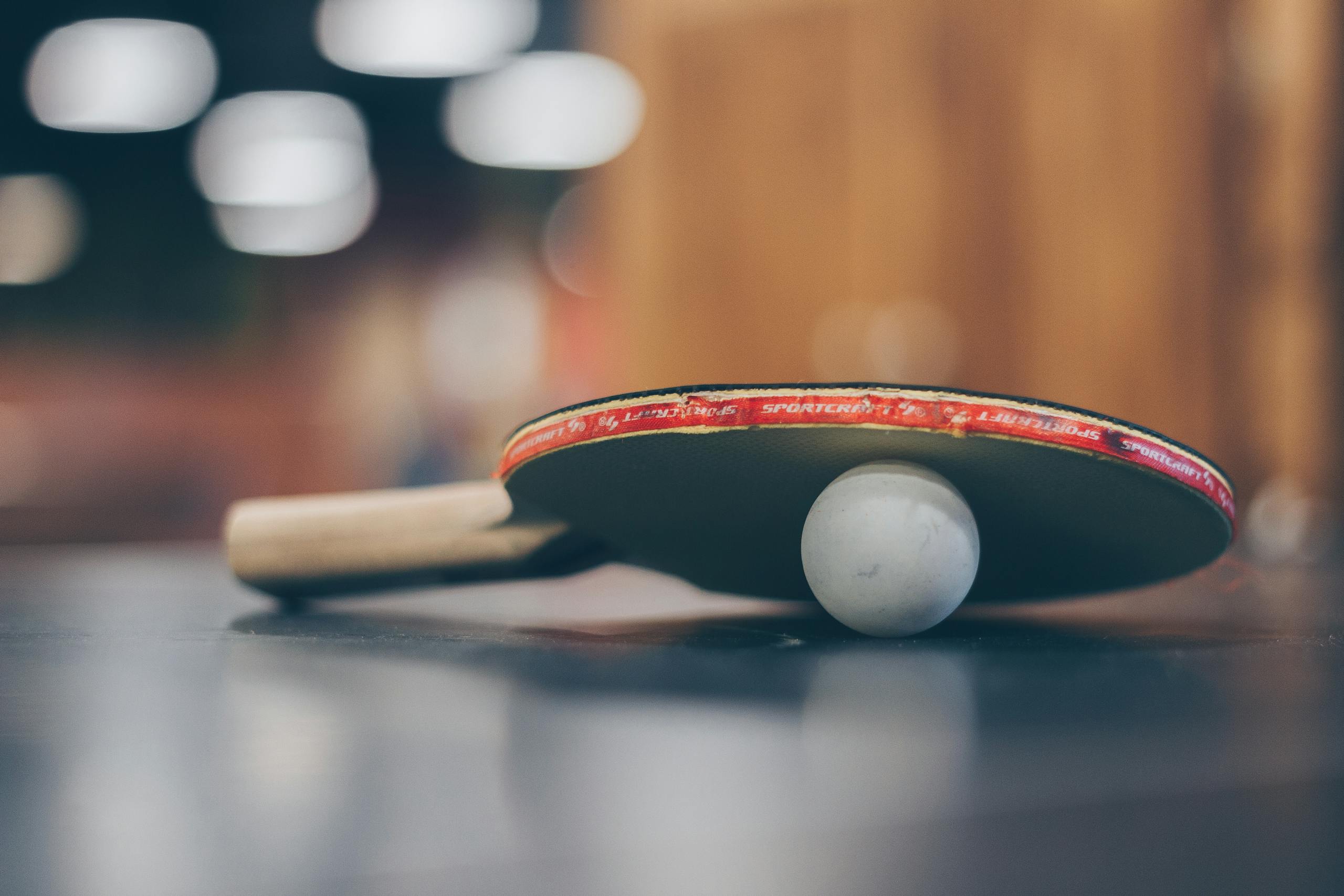 Ping Pong or table tennis racquet and ball angled on dark table tennis table in a stadium setting